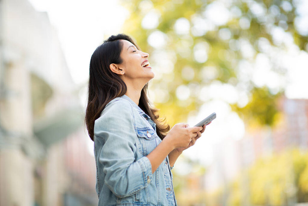 Side portrait of happy young woman holding cellphone in hand - Photo, Image