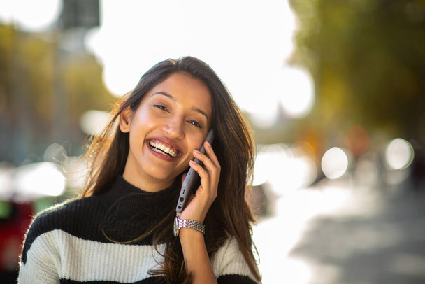 Muotokuva kaunis nuori nainen hymyilee ja puhuu matkapuhelin ulkona kaupungissa - Valokuva, kuva