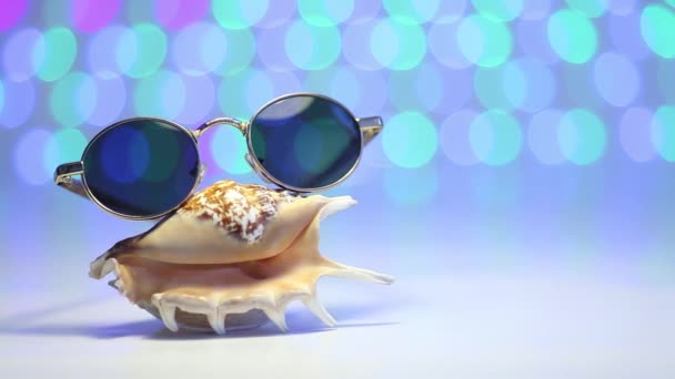 Shell en zonnebril als reizen concept op een onscherpe kleurrijke achtergrond - Video