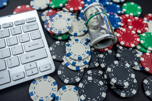 μάρκες πόκερ για πόκερ με τα τραπεζογραμμάτια στριμμένα τοποθετούνται στο πληκτρολόγιο laptop. απομονώνονται σε μαύρο φόντο. Έννοια πόκερ - Φωτογραφία, εικόνα