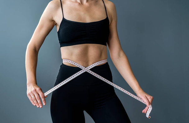 Mujer deportiva en forma de medición con cinta métrica y medición de la cintura después de la dieta aislada sobre fondo gris. Dietética. La pérdida de peso fitness. medición del tamaño - Foto, Imagen