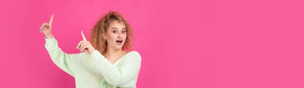 A young girl with curly hair points with a gesture on a studio background. - Foto, Imagen