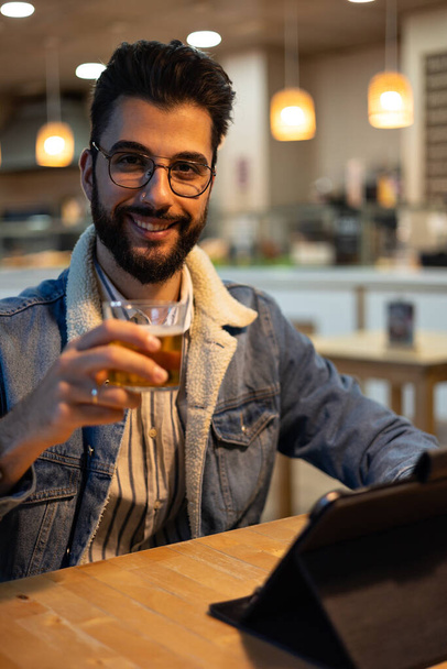 Portrait of young man with beer seated inside a bakery - Foto, Bild