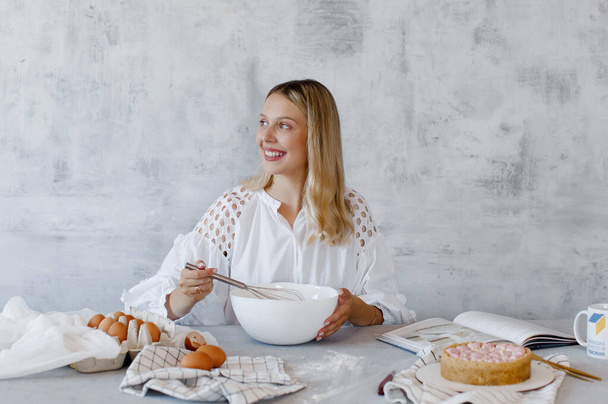 Woman whisking cream with a whisk in a white mixing bowl on a grey background. - Photo, Image