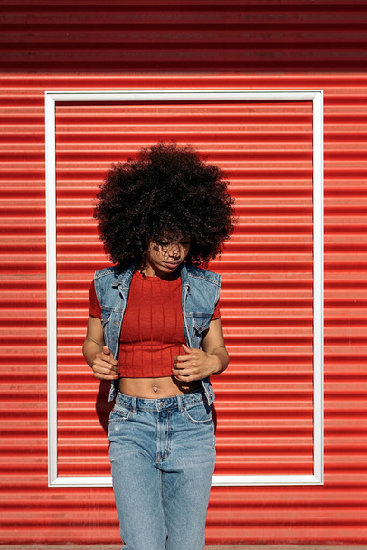 African woman with cool afro hair posing against red background and looking down. - Foto, Imagem