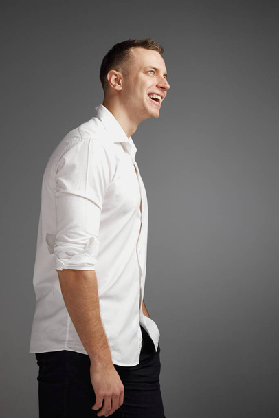 Portrait of young man posing in white shirt isolate dover grey studio background. Cheerfully smiling. Businessman. Concept of mens health, lifestyle, fashion, emotions, well-being. Copy space for ad - Zdjęcie, obraz