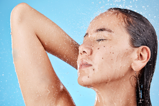 Skincare, beauty and woman in shower on blue background, haircare and hygiene routine in the morning. Model in water splash relax, cleaning hair and face with running water for clean fresh lifestyle - Fotografie, Obrázek