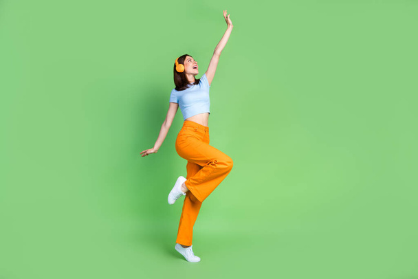 Full body portrait of cheerful gorgeous lady raise arm enjoy new playlist isolated on green color background. - Foto, Imagem