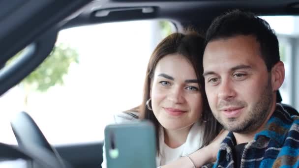 Ένα ερωτευμένο ζευγάρι βγάζει μια selfie φωτογραφία σε ένα καινούριο αυτοκίνητο. Αγορά ηλεκτρικού αυτοκινήτου. Βίντεο 4k - Πλάνα, βίντεο