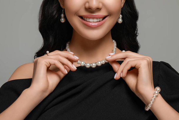 Young woman wearing elegant pearl jewelry on grey background, closeup - Foto, afbeelding