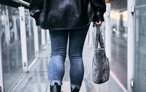 Nahaufnahme Beine in Blue Jeans von einem Latina-Mädchen, das von hinten den gläsernen Gehweg entlang läuft und eine Tasche auf der rechten Seite trägt - Urban concept - Foto, Bild