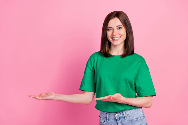Photo portrait of gorgeous young girl palms point empty space present new product wear stylish green look isolated on pink color background. - Fotó, kép