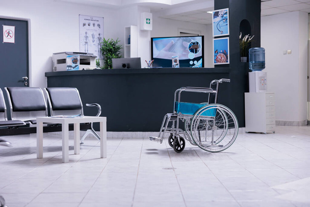 Senki sincs üres váróteremben üres székekkel, személyzet nélküli recepcióval és használaton kívüli bútorokkal. Kerekesszék, ahol nincs lakó a kórház halljában, emberek nélkül. Orvosi szakember nélküli klinika. - Fotó, kép