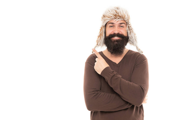 happy bearded man point finger on copy space. mature man with beard in earflap hat. beard hair care. hipster isolated on white. confident guy with moustache wear warm hat. male winter fashion. - 写真・画像