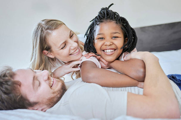 Love, adoption and family portrait, relax and smile on bed in home, happy and support with care. Mother, father and black girl, happiness and freedom in bedroom relaxing, smiling and family home. - Photo, Image