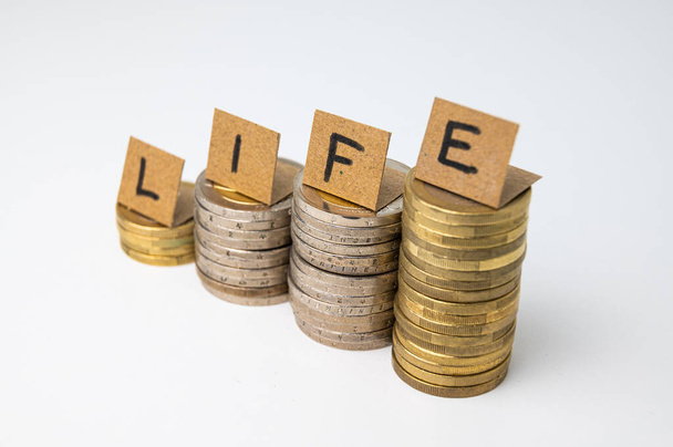 Stapelweise Münzen und vor allem Karten, die das Wort "Leben" buchstabieren. Steigende Lebenshaltungskosten Einkommenssteigerung. - Foto, Bild