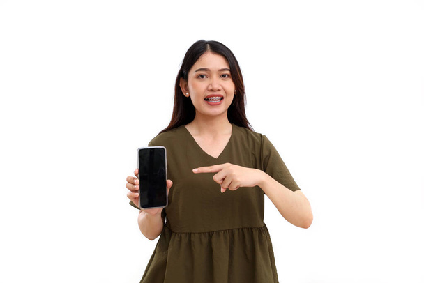 Щаслива молода азіатка стоїть, показуючи або представляючи порожній екран свого мобільного телефону. Ізольовані на білому
 - Фото, зображення