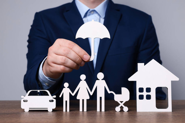 Man holding figure of umbrella above family at wooden table. closeup. Insurance concept - Foto, Imagem