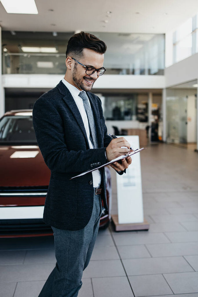 Good looking, cheerful and friendly salesman poses in a car salon or showroom. - Fotografie, Obrázek