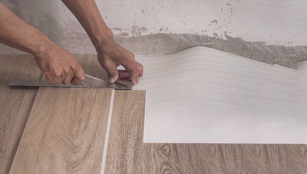 Technik stříhá luxusní vinylové dlaždice s řezačkou, aby položil podlahu, než ji položí na vyrovnávací pěnu. - Fotografie, Obrázek