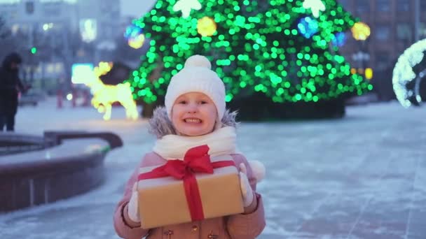 Glückliches kleines Mädchen mit Weihnachtsgeschenk im Winter im Freien an Heiligabend. Weihnachtsgeschenke für die Feiertage - Filmmaterial, Video