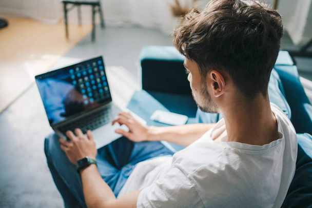 Widok biznesmena siedzącego na kanapie czytającego poranne wiadomości przez laptopa w domu, pracującego w domu. Zwyczajny biznesmen lub freelancer zrelaksowany pracy od - Zdjęcie, obraz