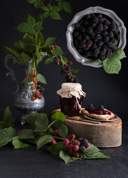 still life with a jar of blackberry jam and bruschettas with soft cheese and berries, decorated with a branch with green leaves,connection of two planes in one image, High quality photo - Photo, Image