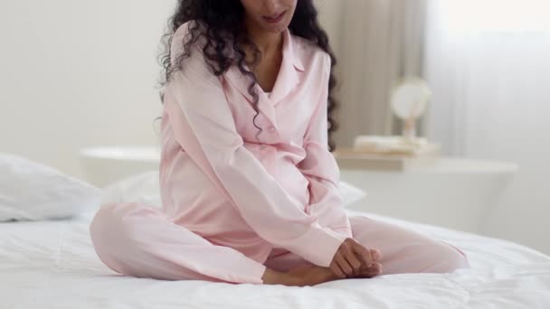 Nuori positiivinen tunnistamaton raskaana oleva nainen hieroo jalkojaan, kärsii aamuturvotuksesta, istuu sängyssä kotona, hidastettuna, vapaa tila - Materiaali, video