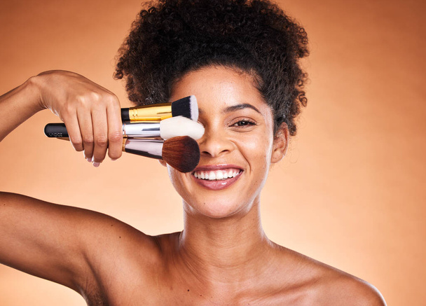 Ομορφιά, μακιγιάζ και πορτρέτο της μαύρης γυναίκας με πινέλα στο στούντιο απομονωμένα σε πορτοκαλί φόντο. Αυτοπεριποίηση, περιποίηση δέρματος και γυναικείο μοντέλο με καλλυντικά, προϊόντα ή πινέλα μακιγιάζ για την αισθητική του δέρματος - Φωτογραφία, εικόνα