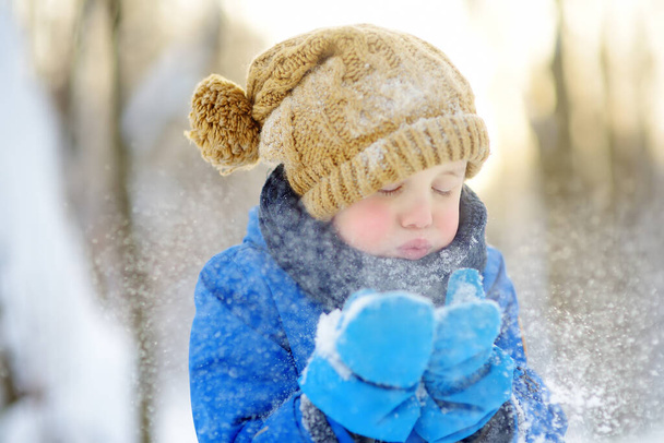 Little boy blowing snow from his hands. Child enjoy walking in the park on snowy day. Baby having fun during snowfall. Outdoor winter activities for family with kids. - Fotografie, Obrázek