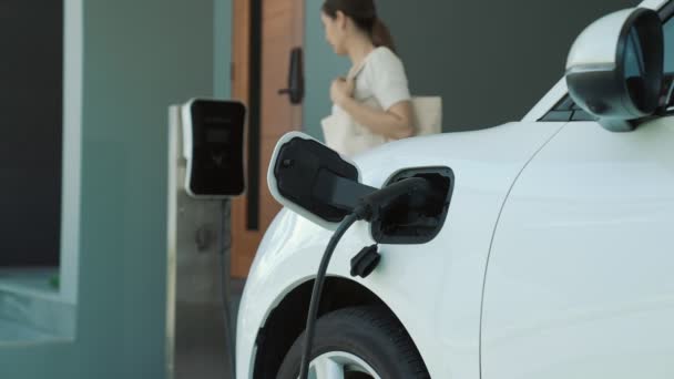Een vrouw haalt de stekker uit de elektrische oplader bij zijn woning. Concept van het gebruik van elektrische voertuigen in een progressieve levensstijl draagt bij tot een schoon en gezond milieu. - Video