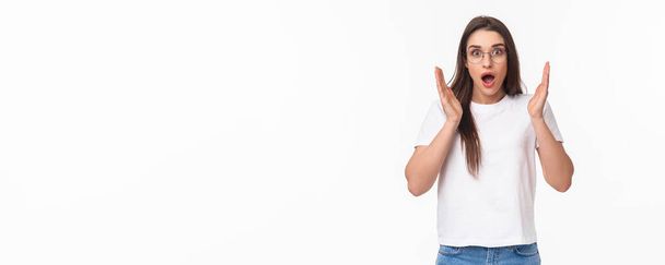 Breaking news. Shocked and astonished young overwhelmed girl in glasses gasping, open mouth and hold hands near face as hear something exciting, standing white background. - Photo, Image