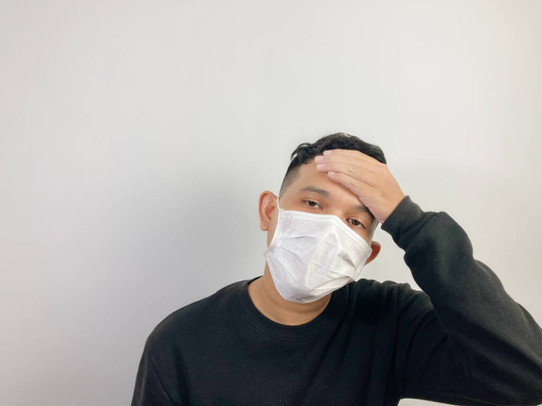  Ein junger asiatischer Mann mit Gesichtsmaske, der üble Kopfschmerzen verspürt, die die Stirn berühren - Foto, Bild