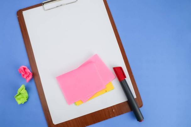 Κενό χαρτί σε ένα ξύλινο σημειωματάριο με κάποιες αυτοκόλλητες σημειώσεις και ένα κόκκινο μαρκαδόρο σε μπλε φόντο. - Φωτογραφία, εικόνα