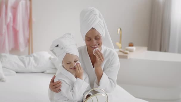 Regeln zur Hautreinigung. Glücklich liebende andere, die ihrer Tochter beibringt, die Gesichtshaut nach dem Duschen mit Wattepads und Lotion zu reinigen, zu Hause gemeinsam lachen, Zeitlupe, freier Raum - Filmmaterial, Video