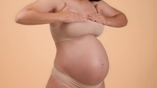 Lähikuva laukaus tunnistamaton raskaana oleva nainen koskettaa hänen tuskallinen rinta, kärsii epämukava tunne, seisoo alusvaatteet yli beige tausta, hidastettuna, vapaa tila - Materiaali, video