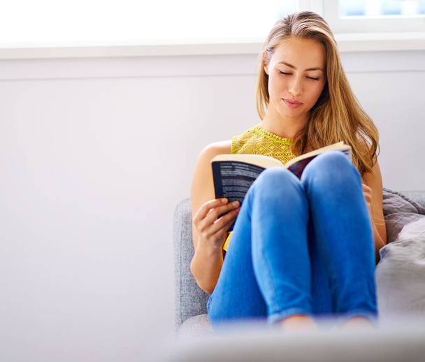 しばらく時間がかかる。家でソファの上で本を読んでいる若い女性が - 写真・画像