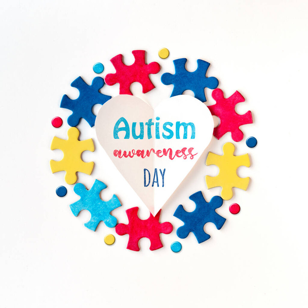 Autism campaign symbols. Colorful puzzle pieces around paper heart with word Autism Awareness Day. Flat lay, top view, square composition. - Photo, Image