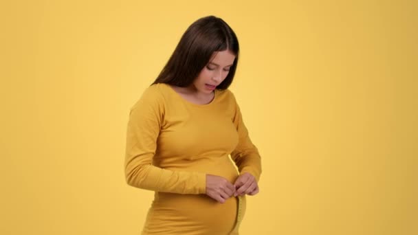 Rychlý růst těhotenství. Mladá těhotná žena měří své velké břicho a cítí šok a neklid, protože extra hmotnost, oranžové studio pozadí, zpomalení pohybu, prázdný prostor - Záběry, video
