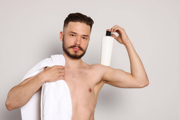 Naked man with towel and bottle of shampoo on light grey background - Photo, image