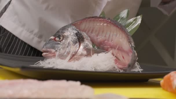 Elaboración de decoración de sushi con daikon, hojas y pescado cortado con cabeza en plato cuadrado negro. Primer plano. - Metraje, vídeo