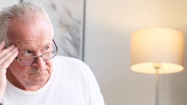 Европейский пожилой пенсионер сидит дома на диване с головной болью и депрессией. Проблемы со здоровьем в старости - Кадры, видео