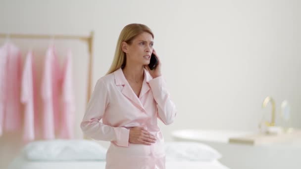 Noodhulp. Bezorgde zwangere vrouw die lijdt aan acute buikpijn, een arts bellen voor medisch advies, thuis staan, slow motion, lege ruimte - Video