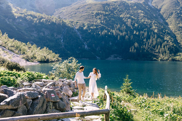 Verliebte Paare gehen auf einem Steinweg. Berge mit Wald und See bedeckt. - Foto, Bild