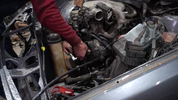 un meccanico smonta un vecchio motore di auto sporca su un ascensore rosso per la riparazione e la messa a punto - Filmati, video