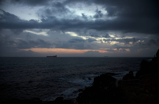 Mar en un día nublado al atardecer con un buque de carga en el horizonte - Foto, imagen