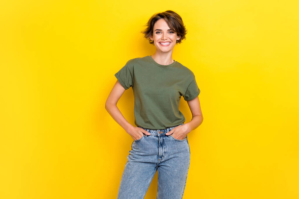 Photo of good mood pretty cute girl with bob hairstyle wear khaki t-shirt hold hands in pockets isolated on yellow color background. - Foto, Bild