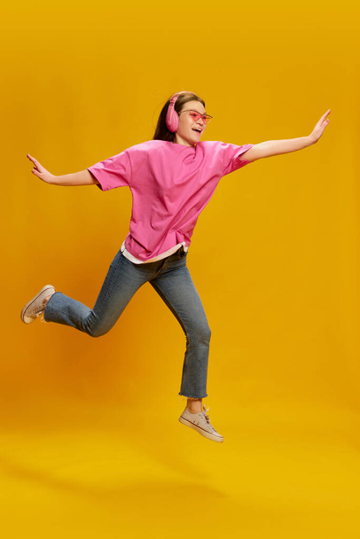 Portrait of young woman in bright casual clothes posing in headphones isolated over yellow background. Positive mood. Concept of youth culture, emotions, facial expression, fashion - Valokuva, kuva
