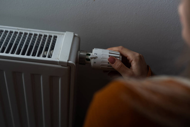 Closeup of woman warming her hands on the heater at home during cold winter days, top view. Female getting warm up her arms over radiator. Concept of heating season, cold weather. - Фото, изображение