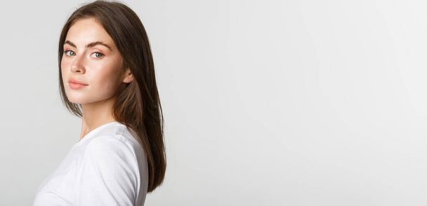 Portrét sebevědomé krásné brunetky žena otáčení tvář na kameru s zasněným vzhledem, bílé pozadí. - Fotografie, Obrázek
